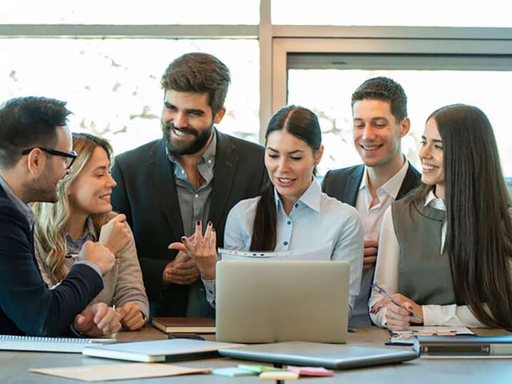 Gruppo di persone in un ufficio sorridenti davanti ad un computer laptop